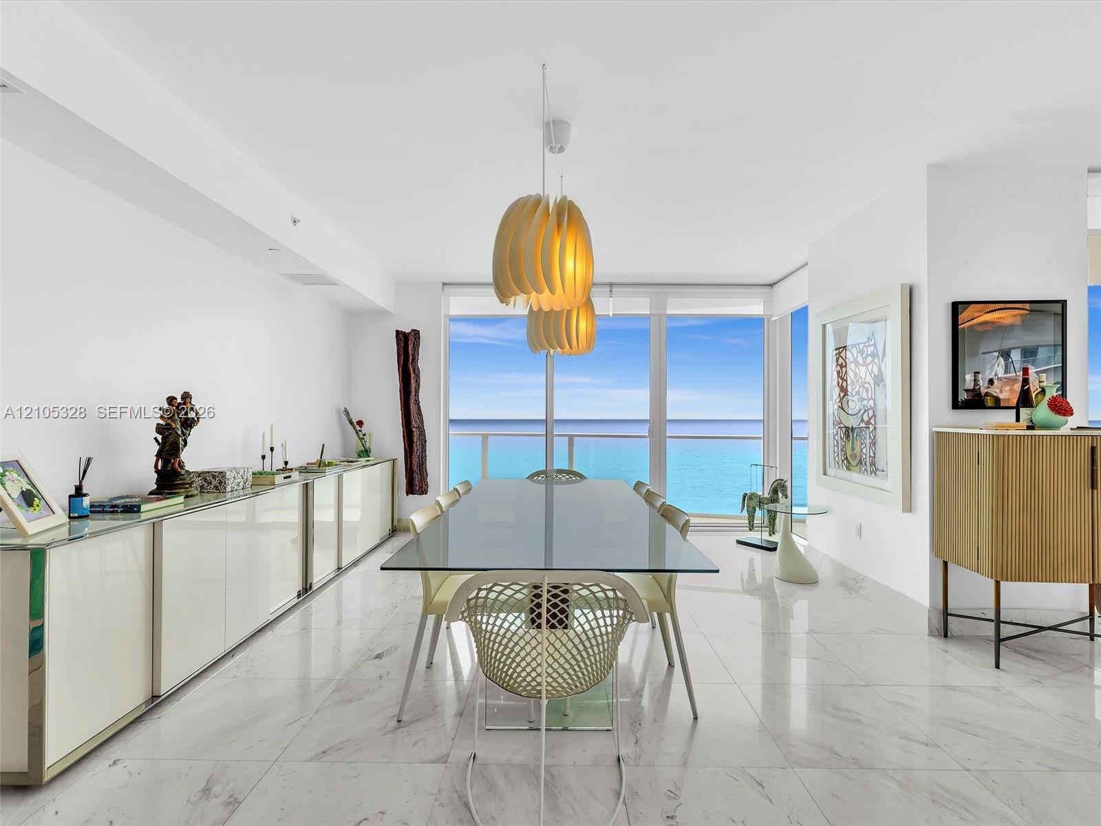 Elegant dining area featuring floor-to-ceiling glass doors and windows, large-format tile flooring, contemporary pendant lighting, and a glass-top din