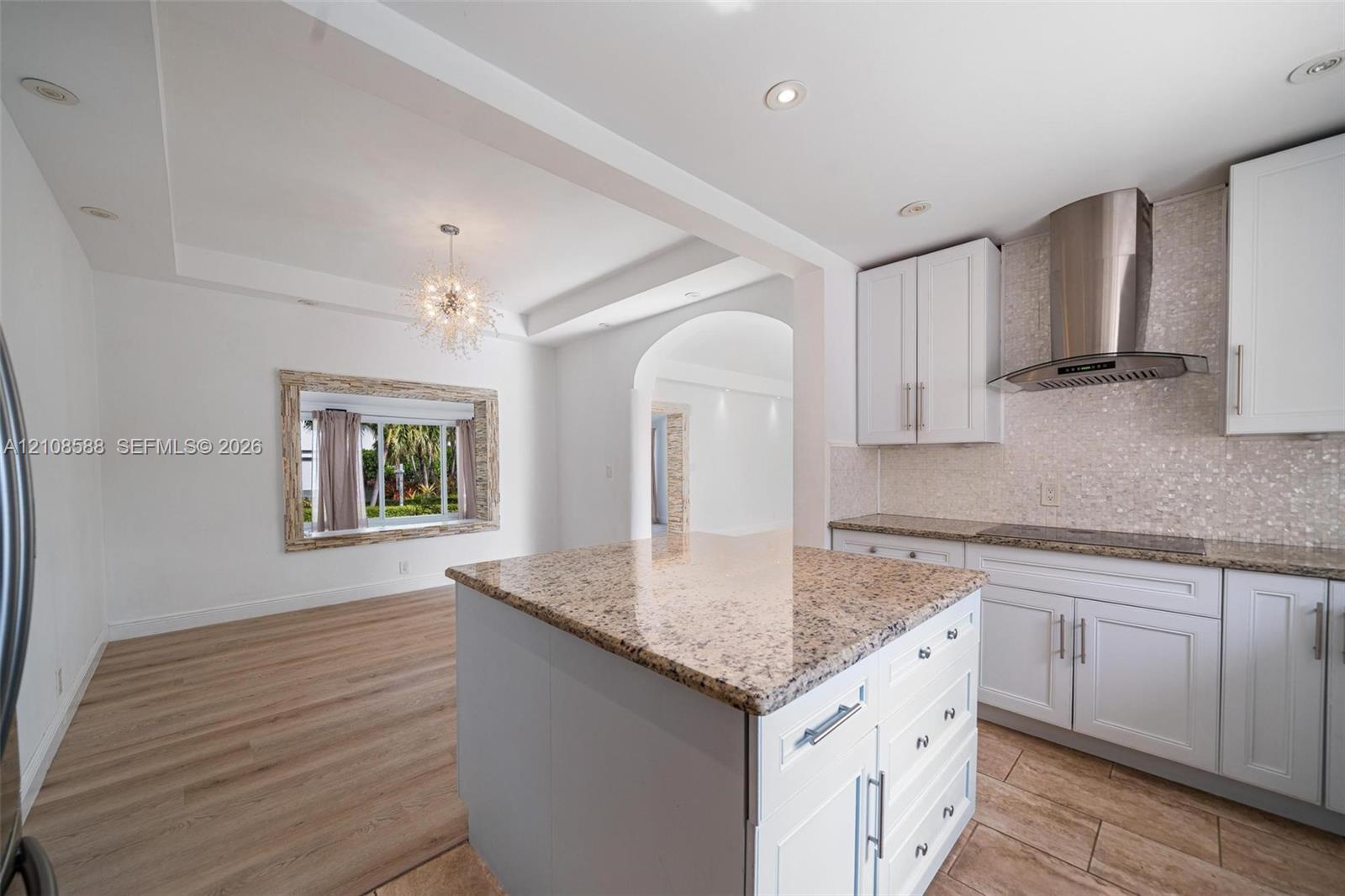 Kitchen featuring white cabinetry, stone-surfaced center island, stainless steel chimney-style range hood, recessed lighting, and wood-finish flooring