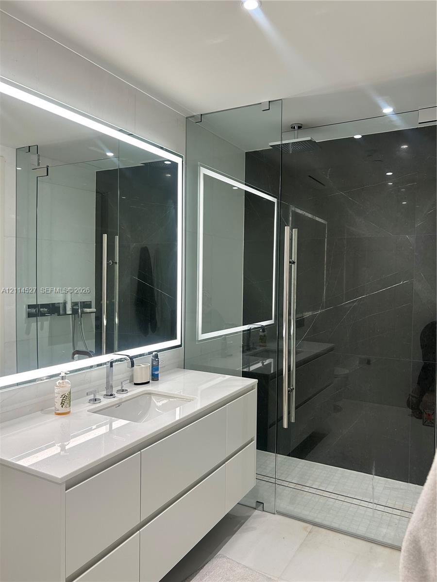 Wall-mounted floating vanity with integrated rectangular sink and stone-surface countertop, frameless glass-enclosed shower featuring large-format dar