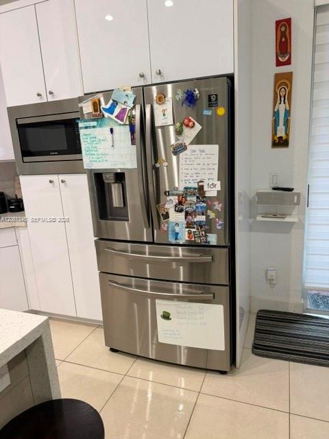 Stainless steel refrigerator, built-in microwave, white cabinetry, recessed lighting, and tile flooring