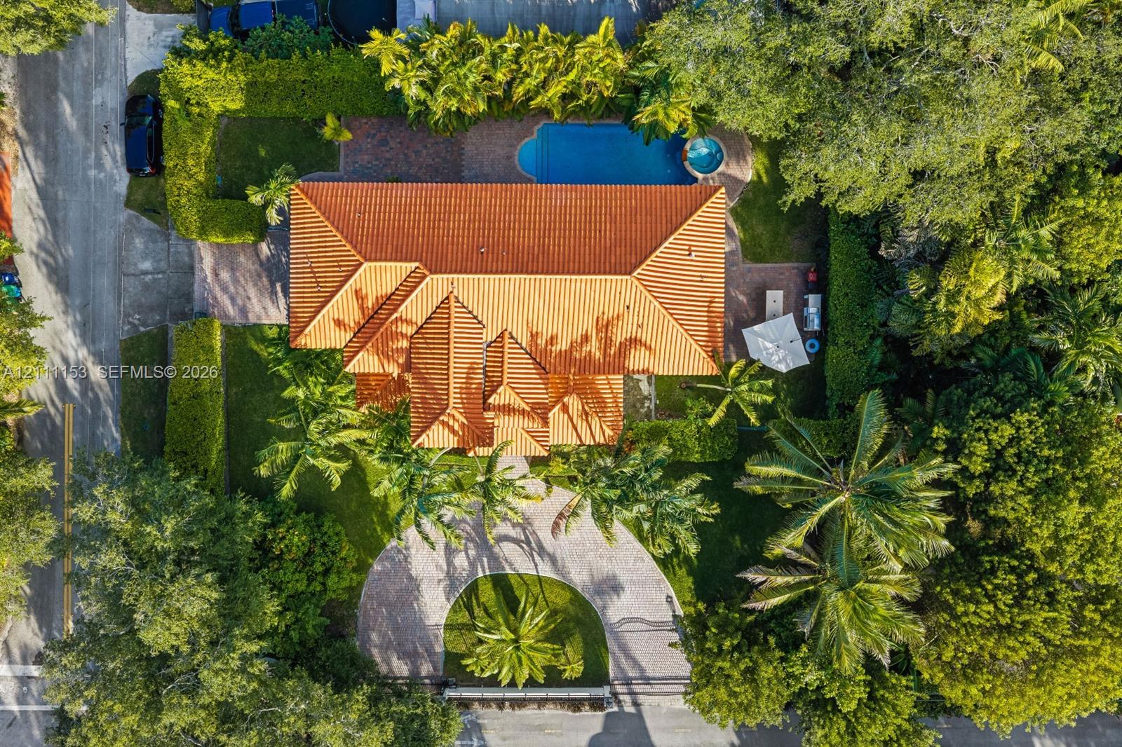 Aerial perspective featuring a multi-gabled clay tile roof, a circular paved driveway, a swimming pool, a separate spa, and mature landscaping