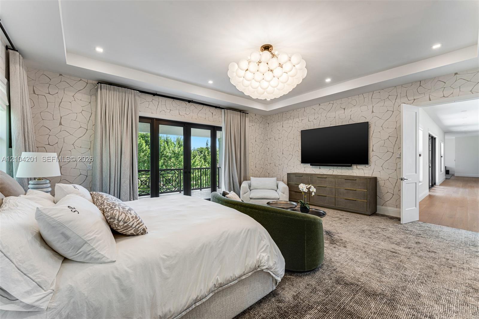 Tray ceiling with recessed lighting, custom multi-globe chandelier, patterned wall treatment, and floor-to-ceiling glass panel doors opening to a balc