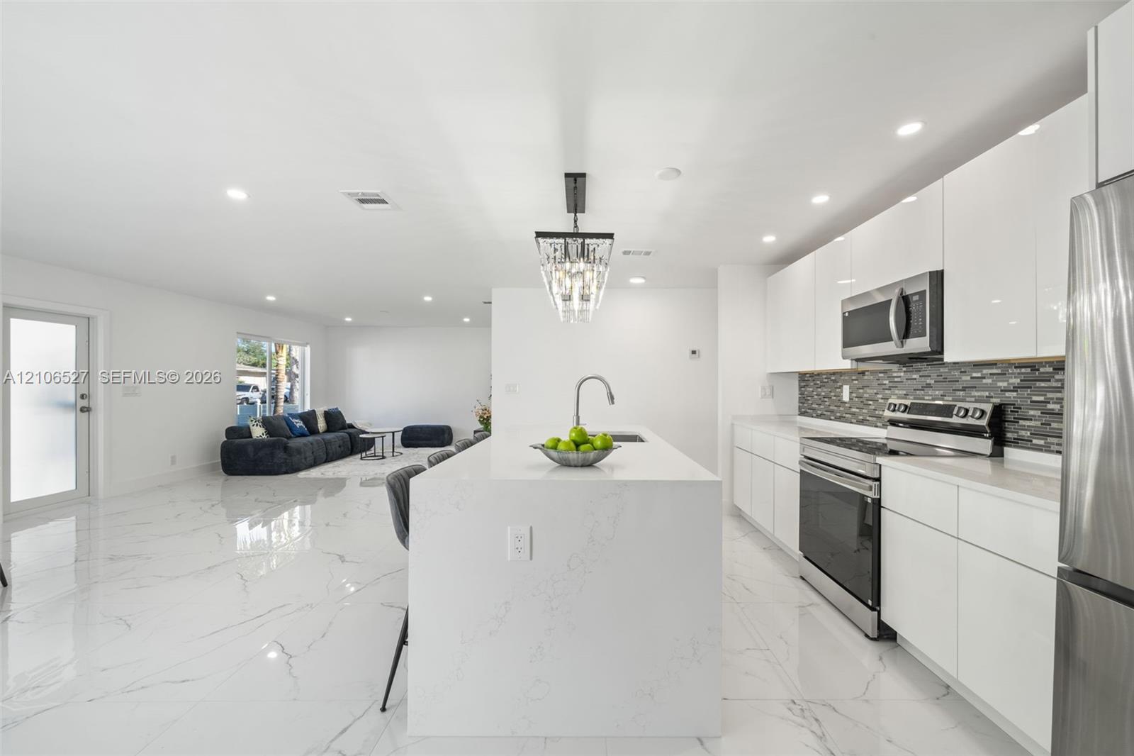 Kitchen featuring white flat-panel cabinetry, a central island with a solid-surface waterfall countertop, stainless steel appliances, a glass-tile bac