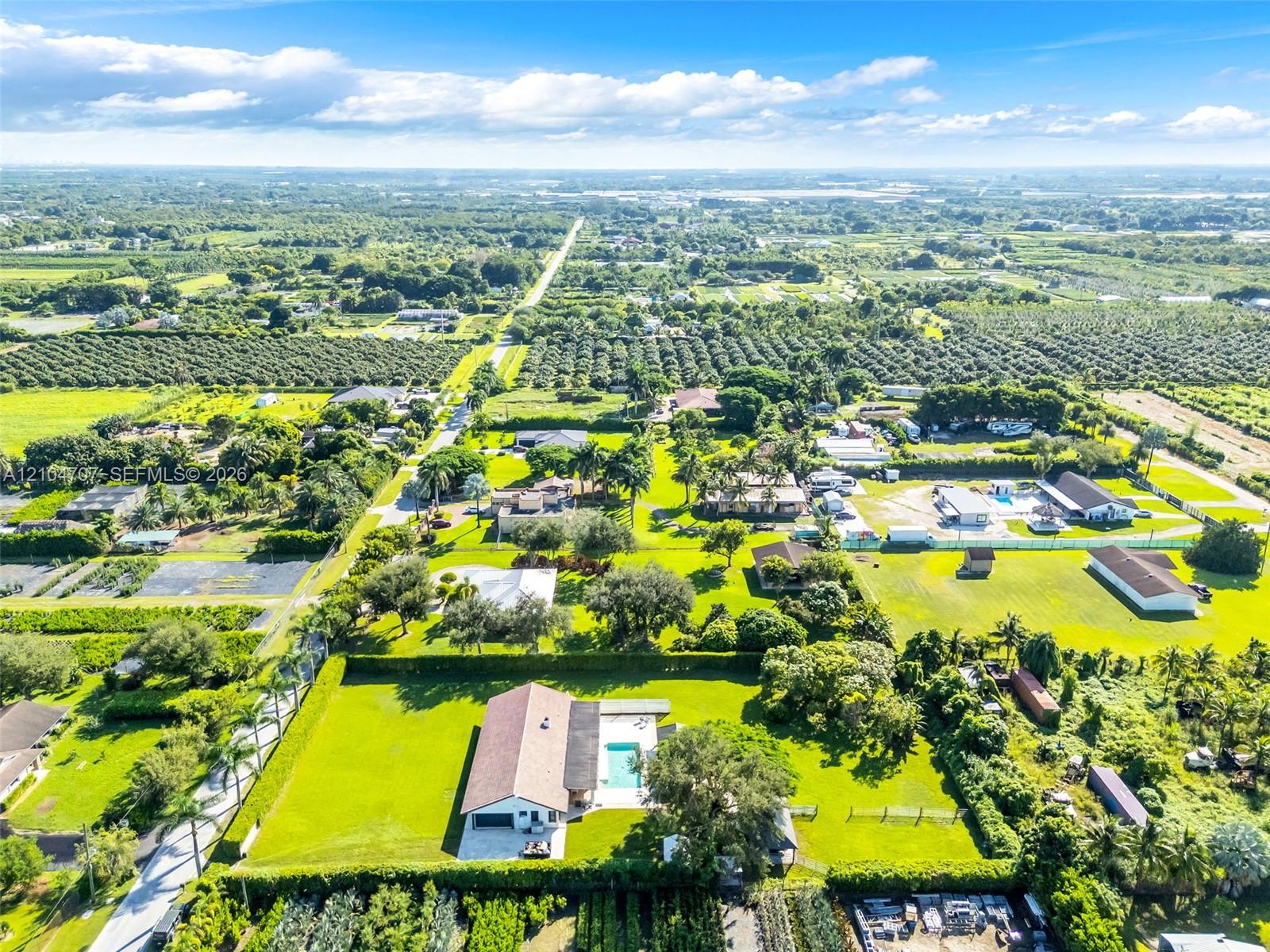 Aerial perspective of a sprawling property featuring expansive landscaped grounds, mature palm trees, a dedicated swimming pool, and an attached multi