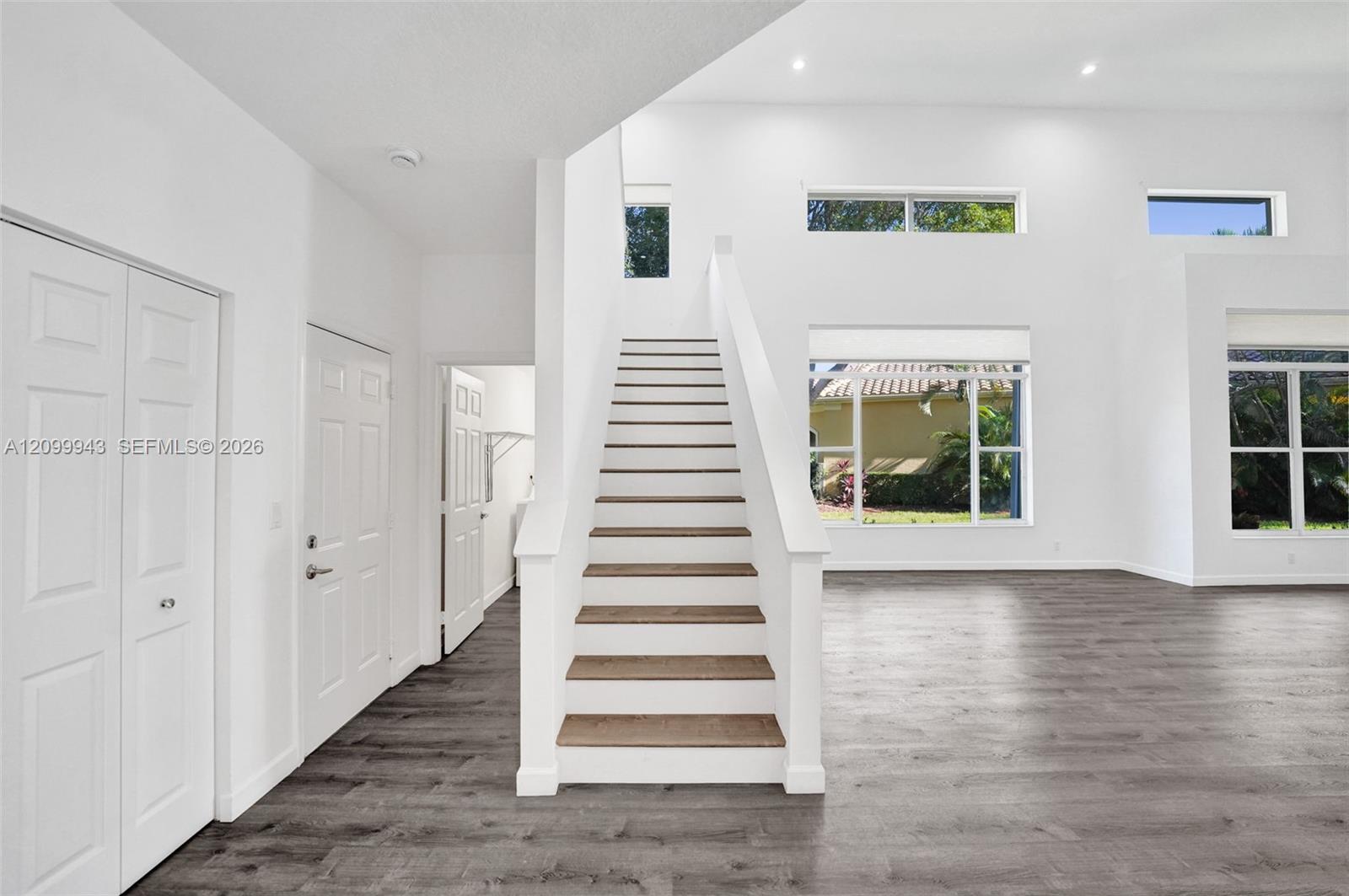 Double-height ceiling, wood-finish flooring, staircase with wood-finish treads, and multiple windows providing natural light