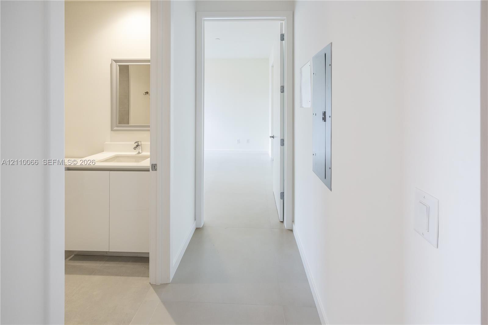 Hallway featuring neutral-toned flooring, white cabinetry with integrated countertop, a rectangular mirror, and a wall-mounted electrical panel