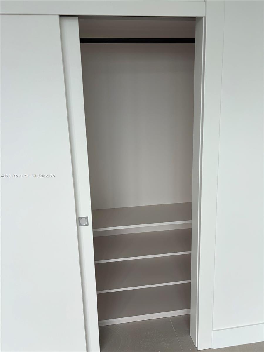 Storage space featuring a white sliding door, square chrome-finish hardware, three built-in shelves, and a horizontal hanging rod