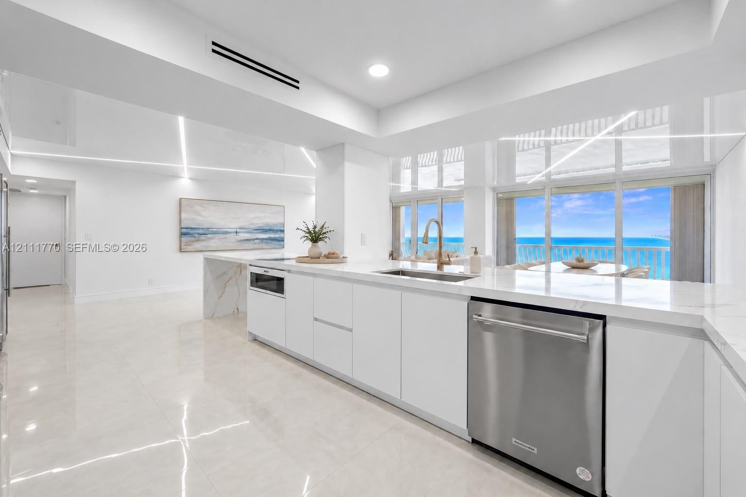 Modern kitchen featuring sleek white cabinetry, stone-finish countertops, stainless steel appliances, and large-format tile flooring, complete with ex
