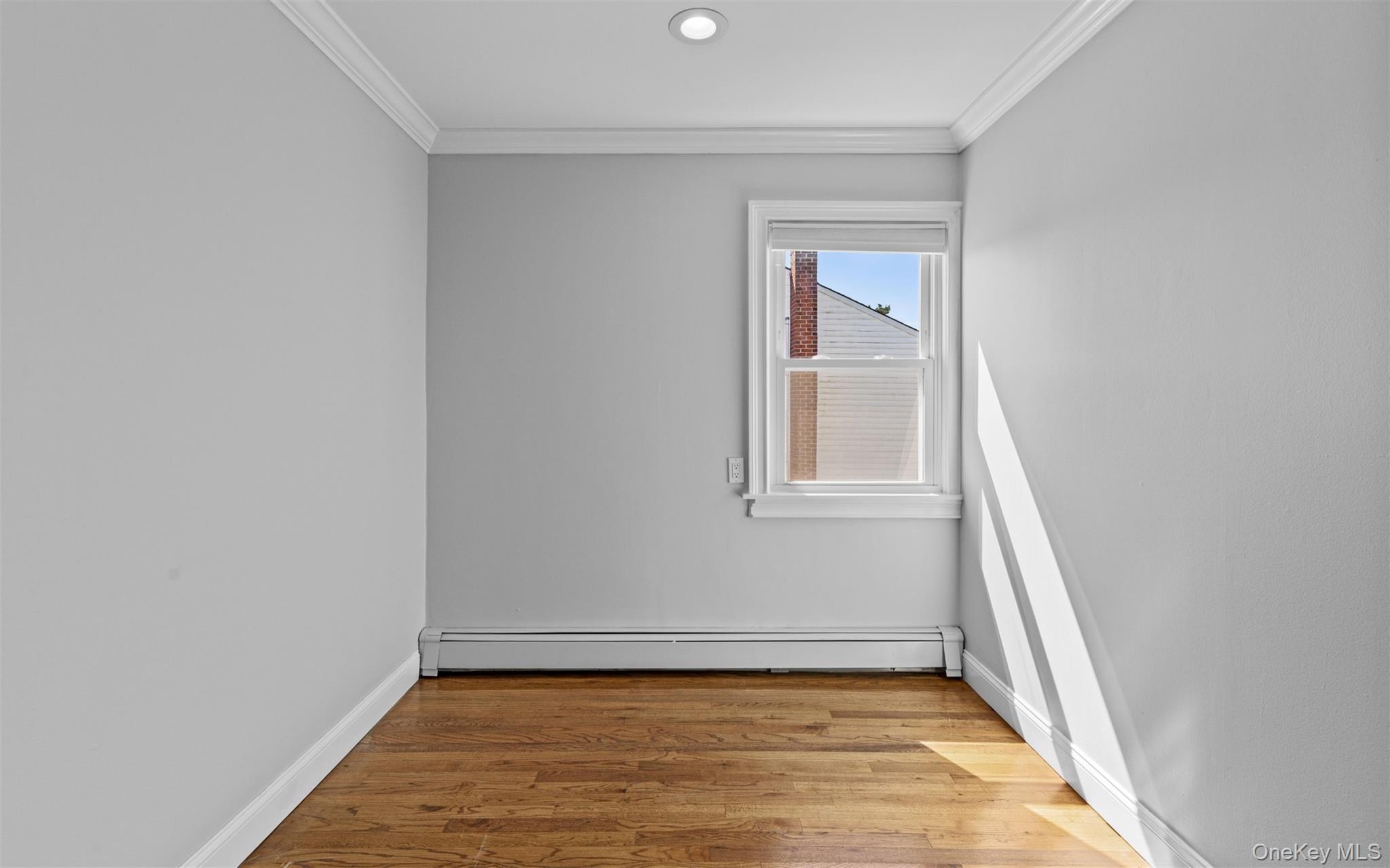 Recessed ceiling lighting, crown molding, wood-finish flooring, single window, and a wall-mounted radiator