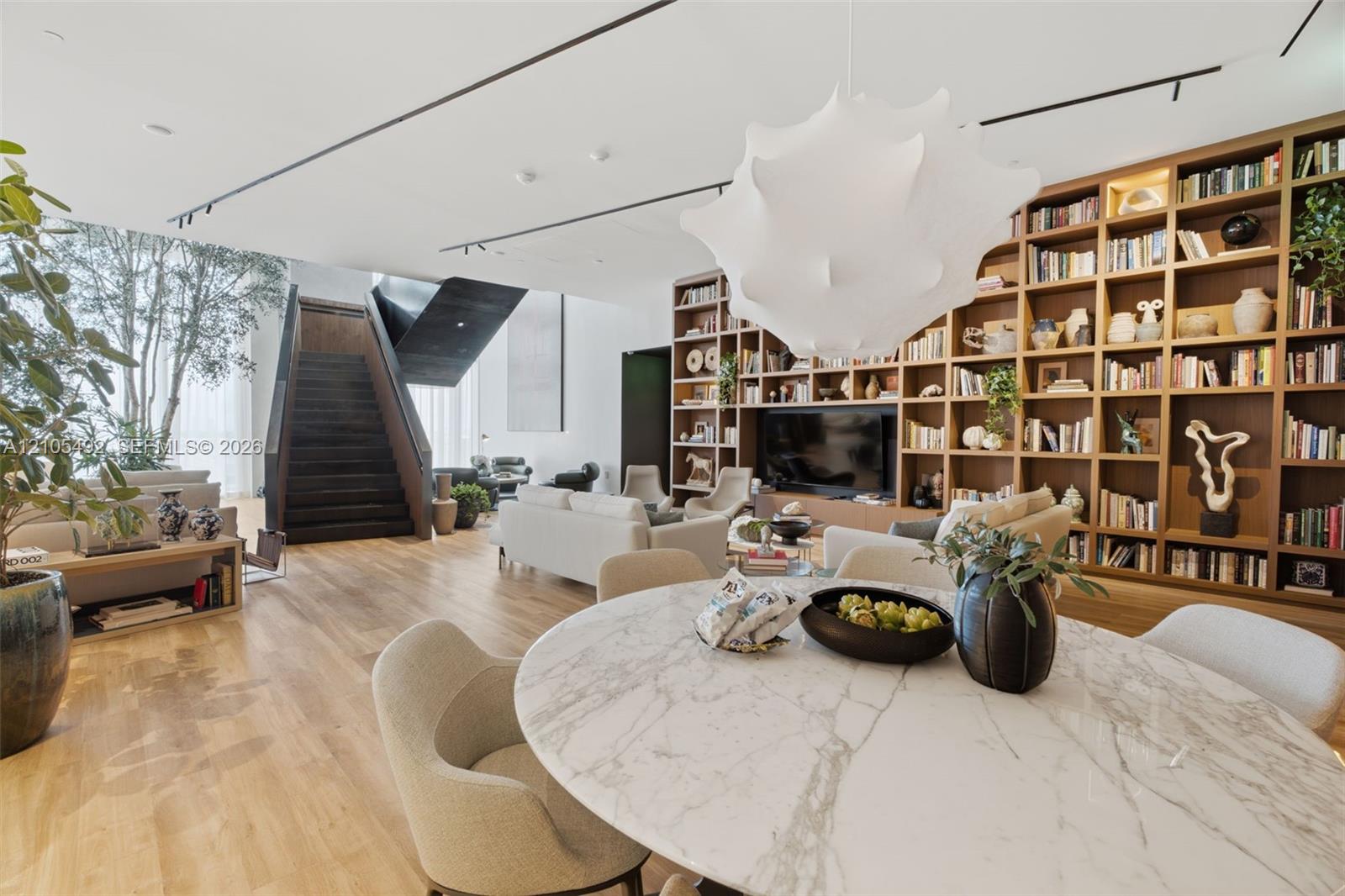 Open-concept interior featuring wood-finish flooring, a floor-to-ceiling built-in wooden bookcase, an architectural staircase with dark metal detailin