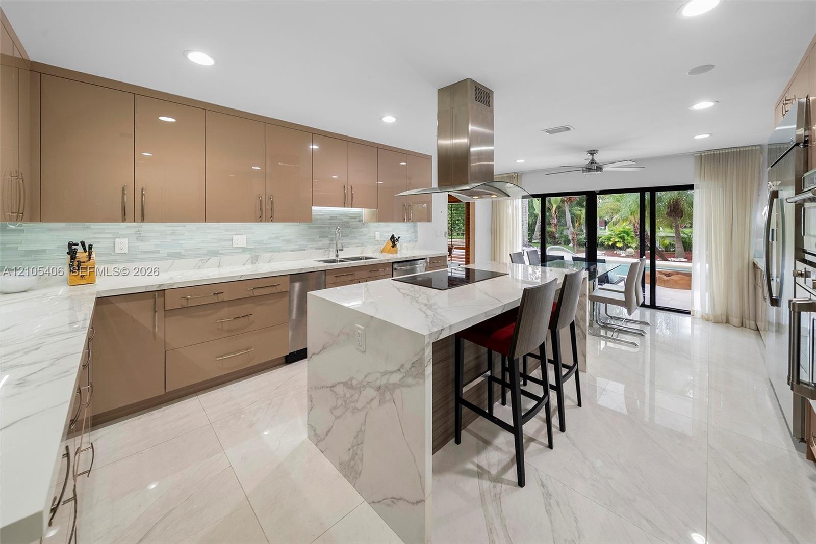 Sleek kitchen featuring an expansive island with waterfall edge, full suite of stainless steel appliances, modern cabinetry, and glass sliding doors