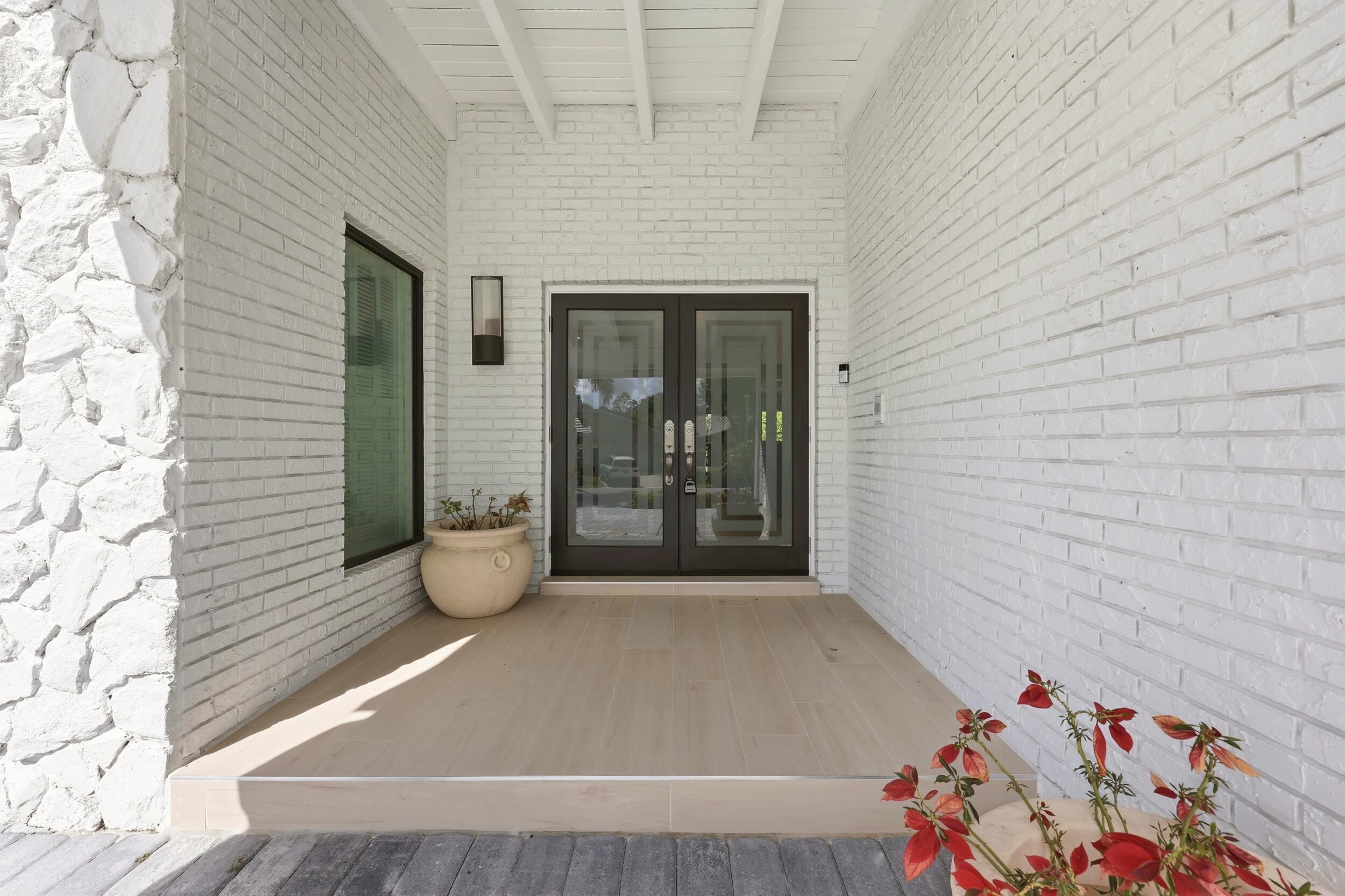 A welcoming covered entry beautifully blends timeless Old Florida charm with sophisticated modern design. Painted white brick and natural stone create