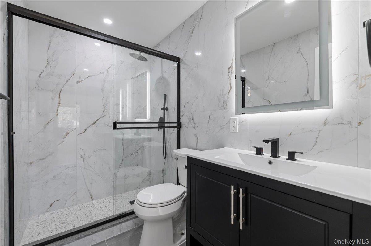 Bathroom featuring vanity, a marble finish shower, tile walls, and recessed lighting