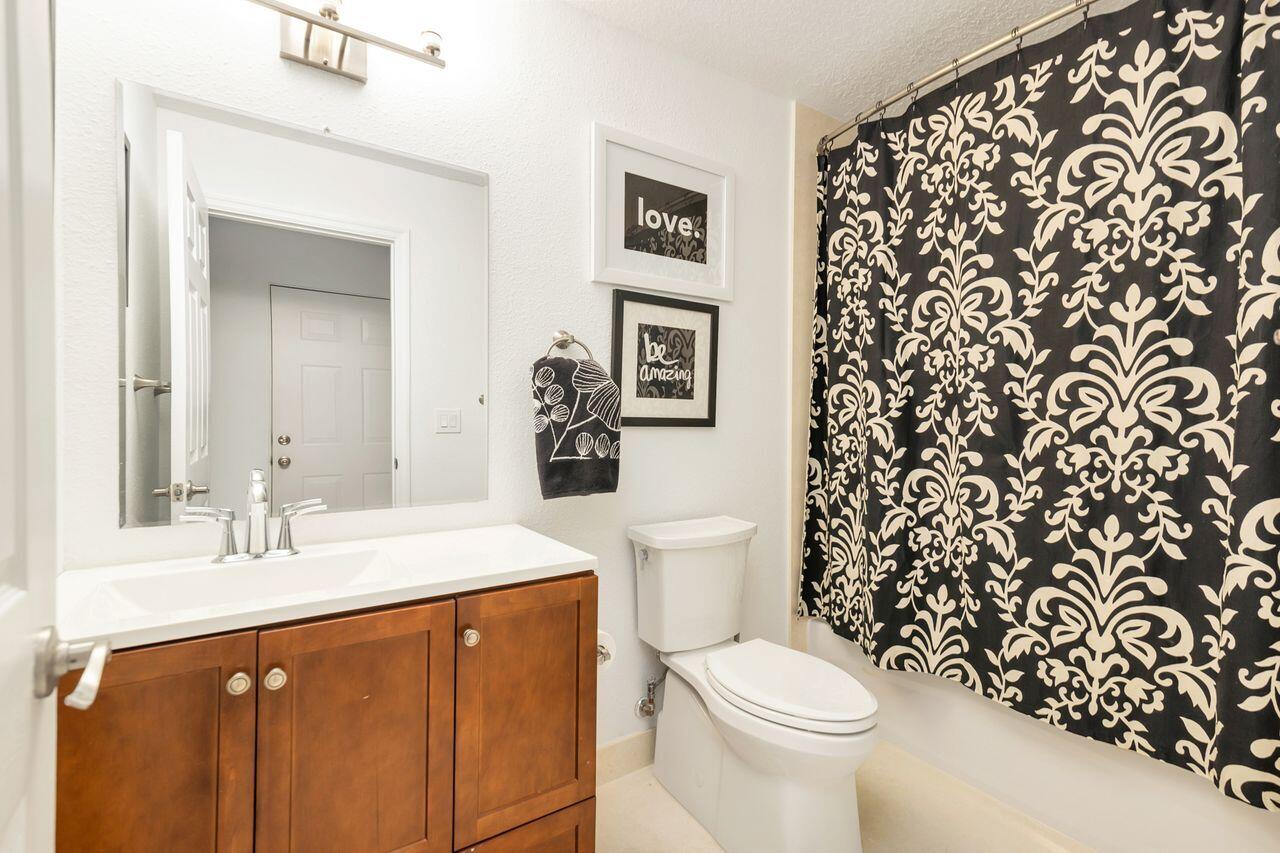 Bathroom featuring a wood-finish vanity with a white countertop and integrated sink, brushed nickel faucet, wall-mounted mirror, and overhead vanity l