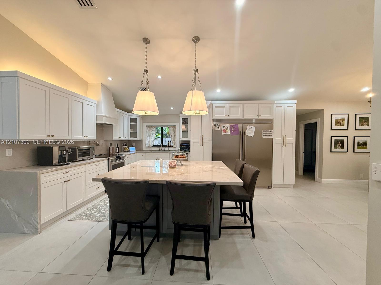 Kitchen featuring white cabinetry, a central island with a stone countertop, stainless steel refrigerator, stone-style flooring, and dual pendant ligh