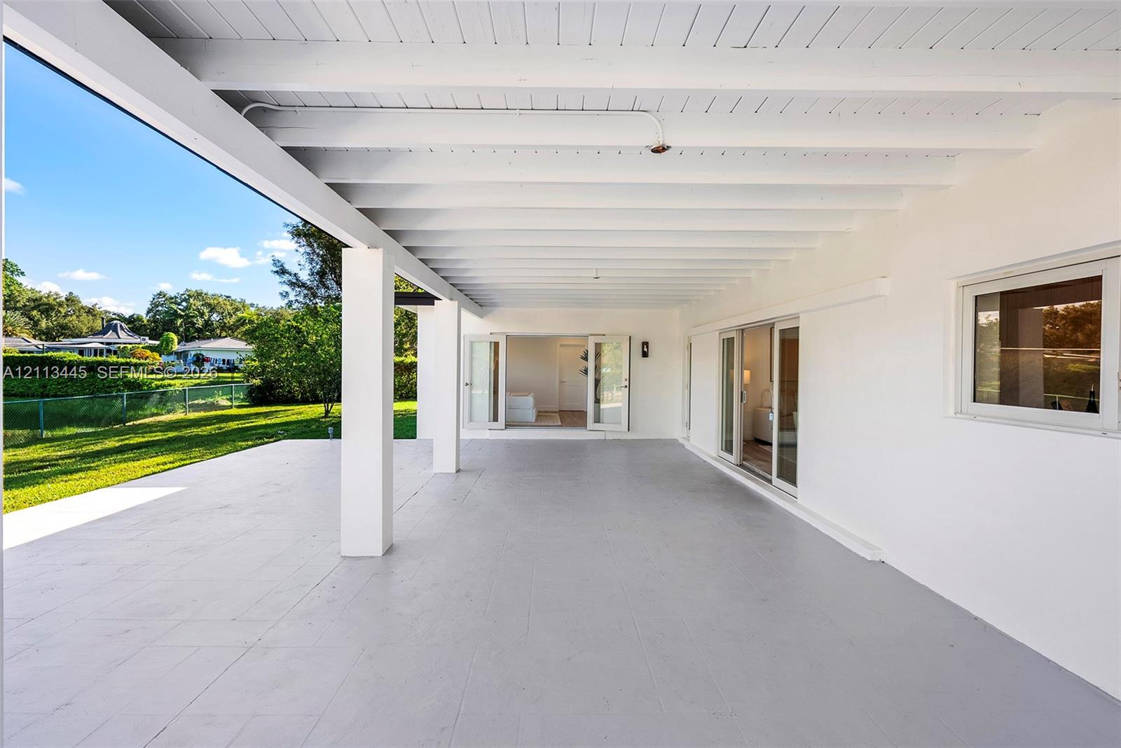 Covered patio featuring a painted wood-beam ceiling, concrete flooring, sliding glass doors, and French doors