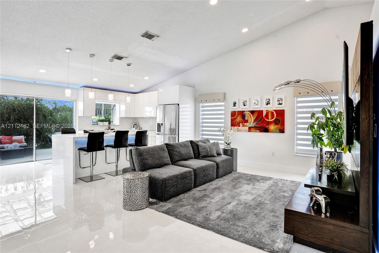 Open-concept interior featuring vaulted ceilings, recessed lighting, white cabinetry with integrated appliances, a kitchen island with stone-finish co