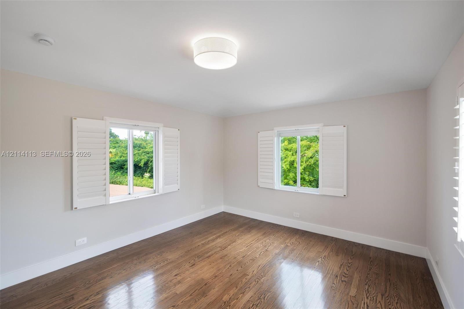 Neutral interior featuring wood-finish flooring, white plantation shutters, and a central drum flush-mount light fixture