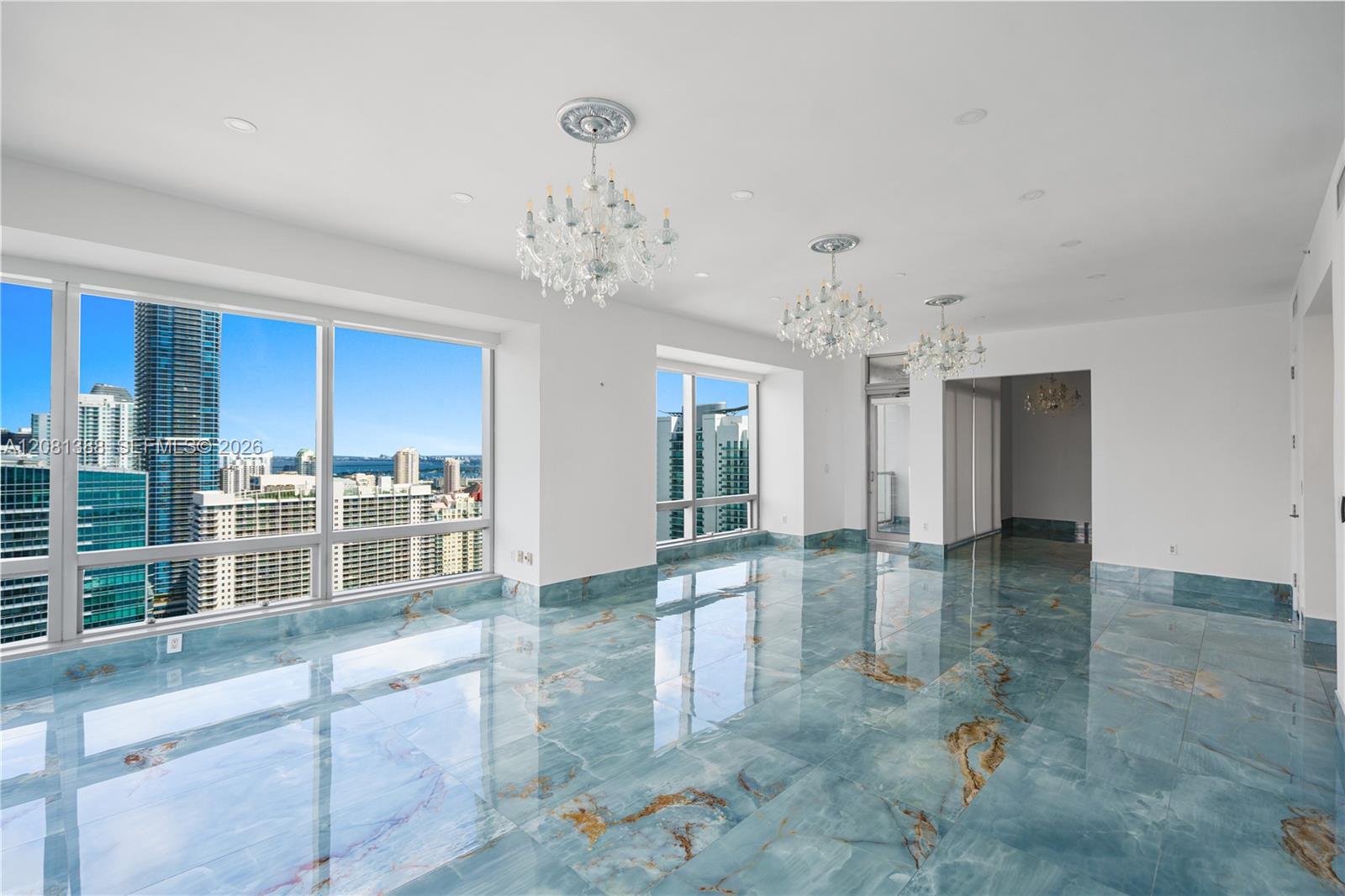 Polished stone flooring with blue and gold veining, floor-to-ceiling windows, three decorative crystal chandeliers with ceiling medallions, and recess