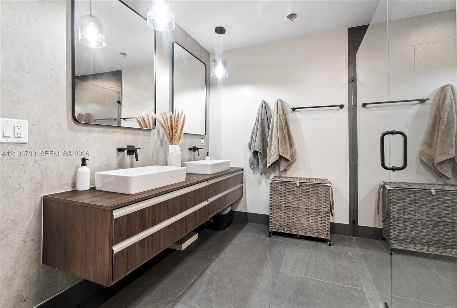 Floating wood-finish double vanity featuring white vessel sinks, matte black wall-mounted faucets, rectangular mirrors, and large-format tile flooring