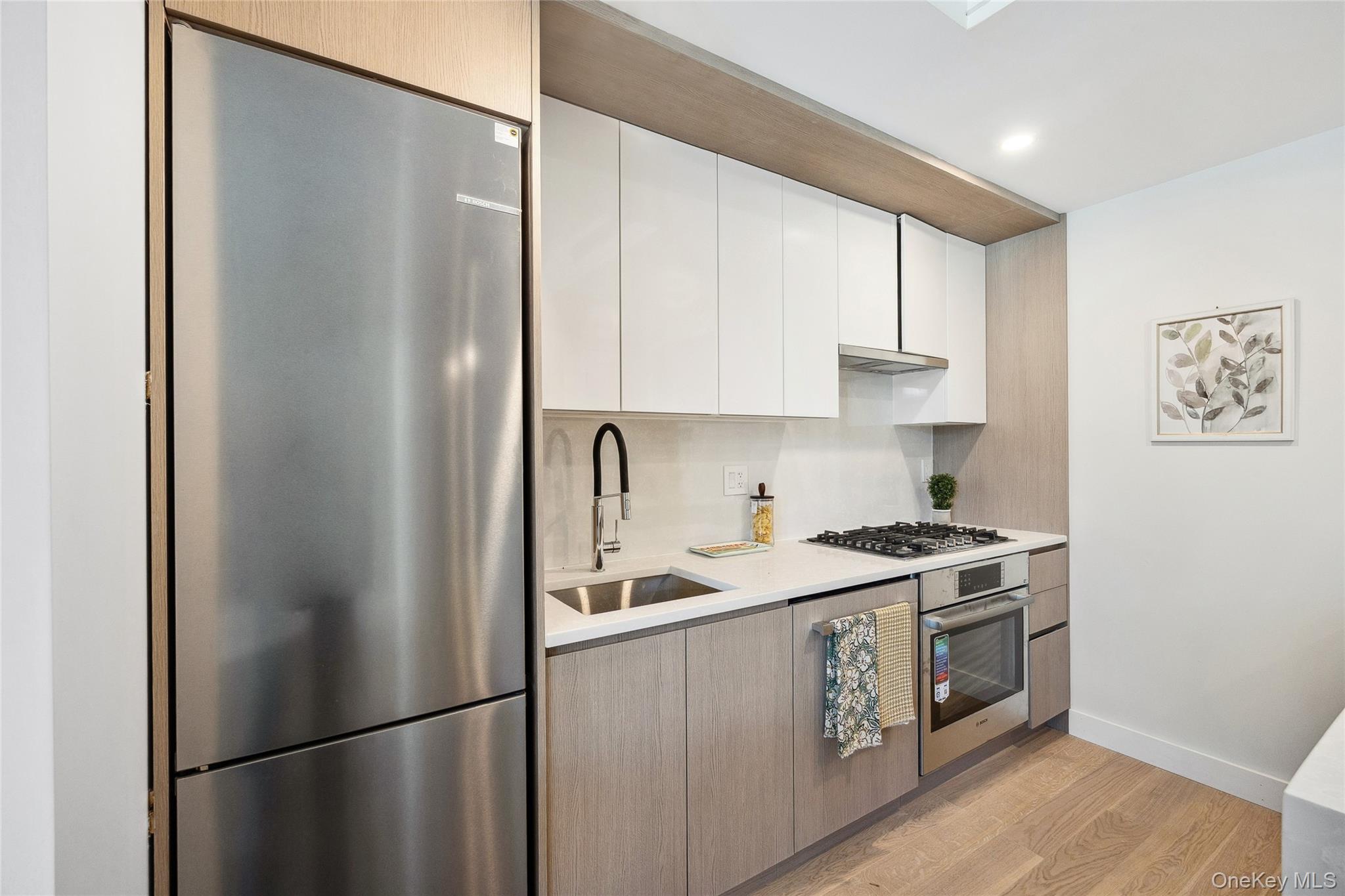 Kitchen with appliances with stainless steel finishes, a sink, light countertops, light wood-style flooring, and white cabinetry