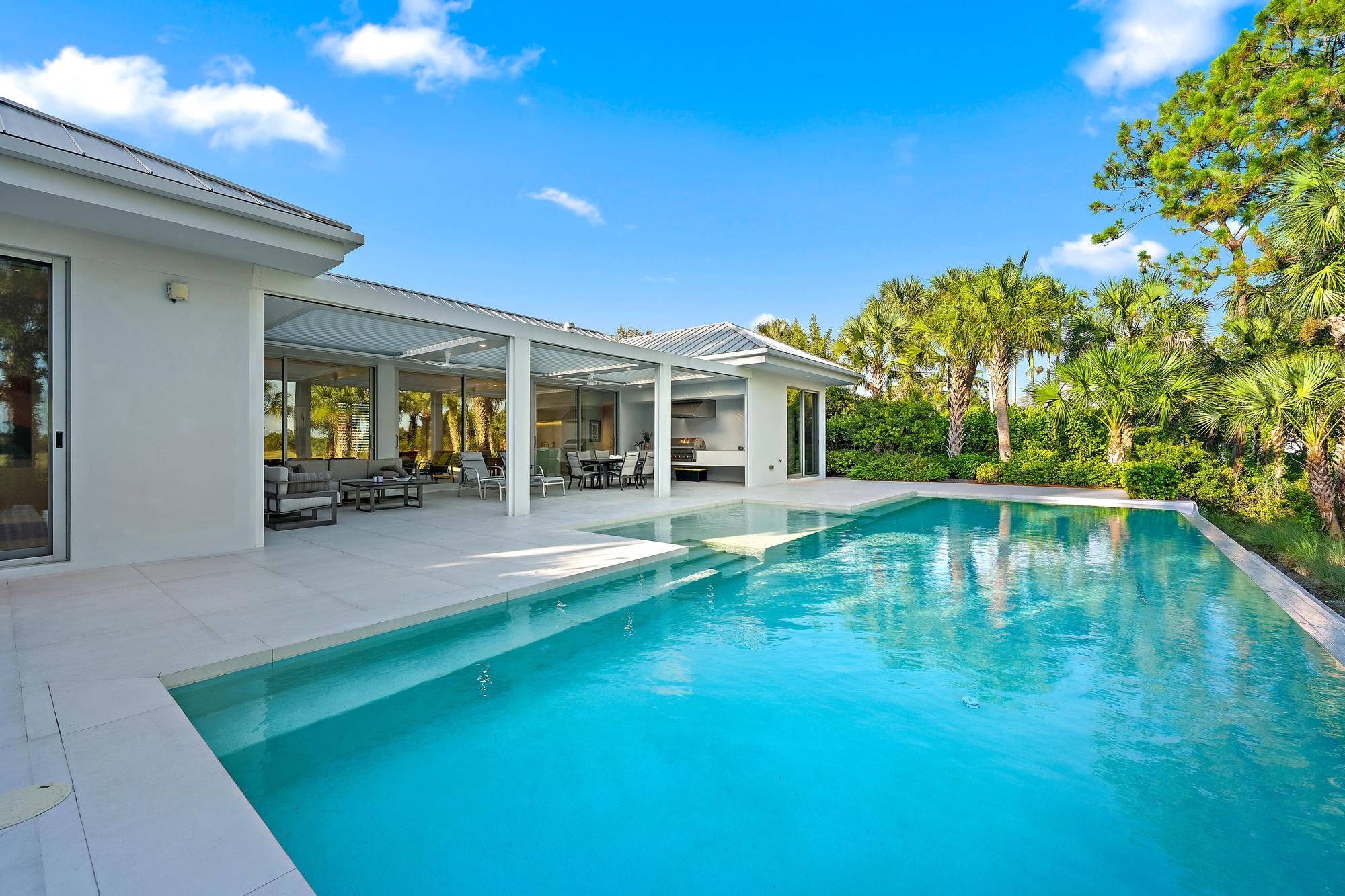 Resort-style saltwater swimming pool with turquoise finish and generous sun deck, anchored by a modern white pergola structure and expansive covered l