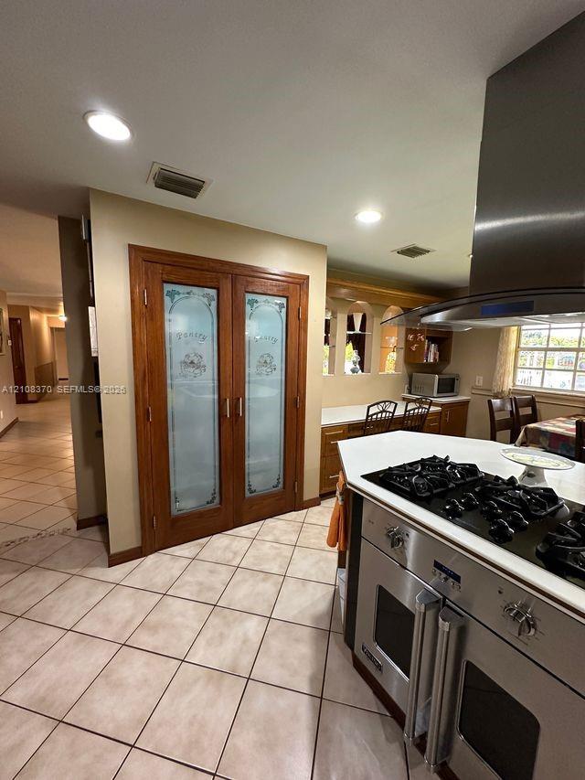 Kitchen featuring double doors with frosted glass panels, stainless steel gas range with overhead vent hood, ceramic tile flooring, and built-in cabin
