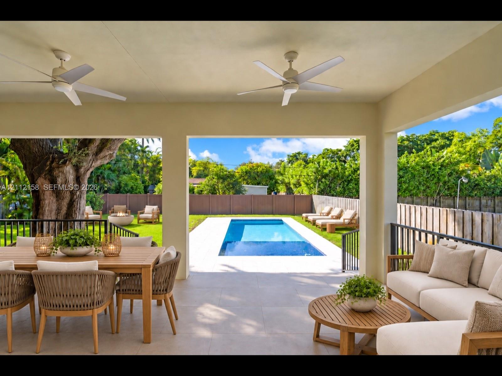 Spacious covered patio with stone-look tile and ceiling fans, overlooking the rectangular pool — ideal for entertaining or relaxing in the shade