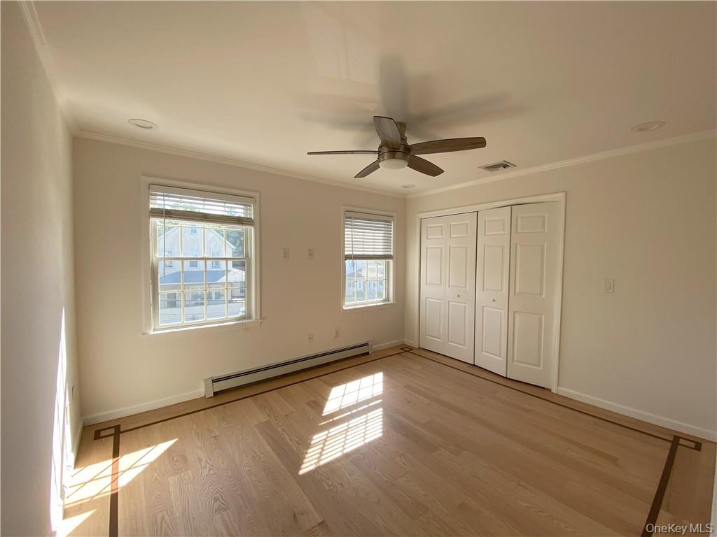Unfurnished bedroom featuring ceiling fan, light hardwood / wood-style flooring, baseboard heating, and crown molding