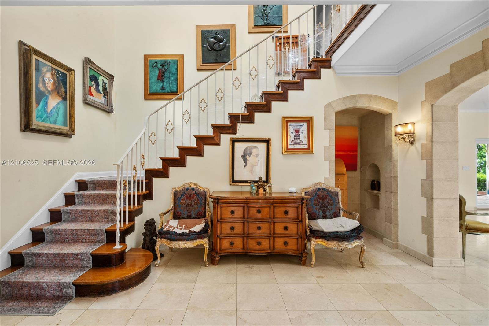 Staircase featuring wood treads, ornate metal railings, and stone-tiled flooring, complemented by an arched stone-trimmed doorway