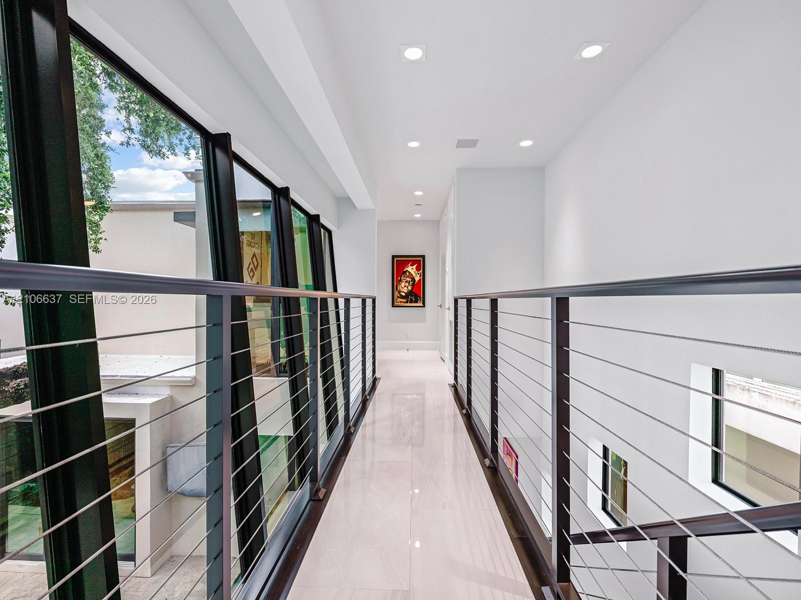 Hallway featuring polished light-toned flooring, recessed ceiling lighting, and a metal cable railing system with dark-finish posts, complemented by f