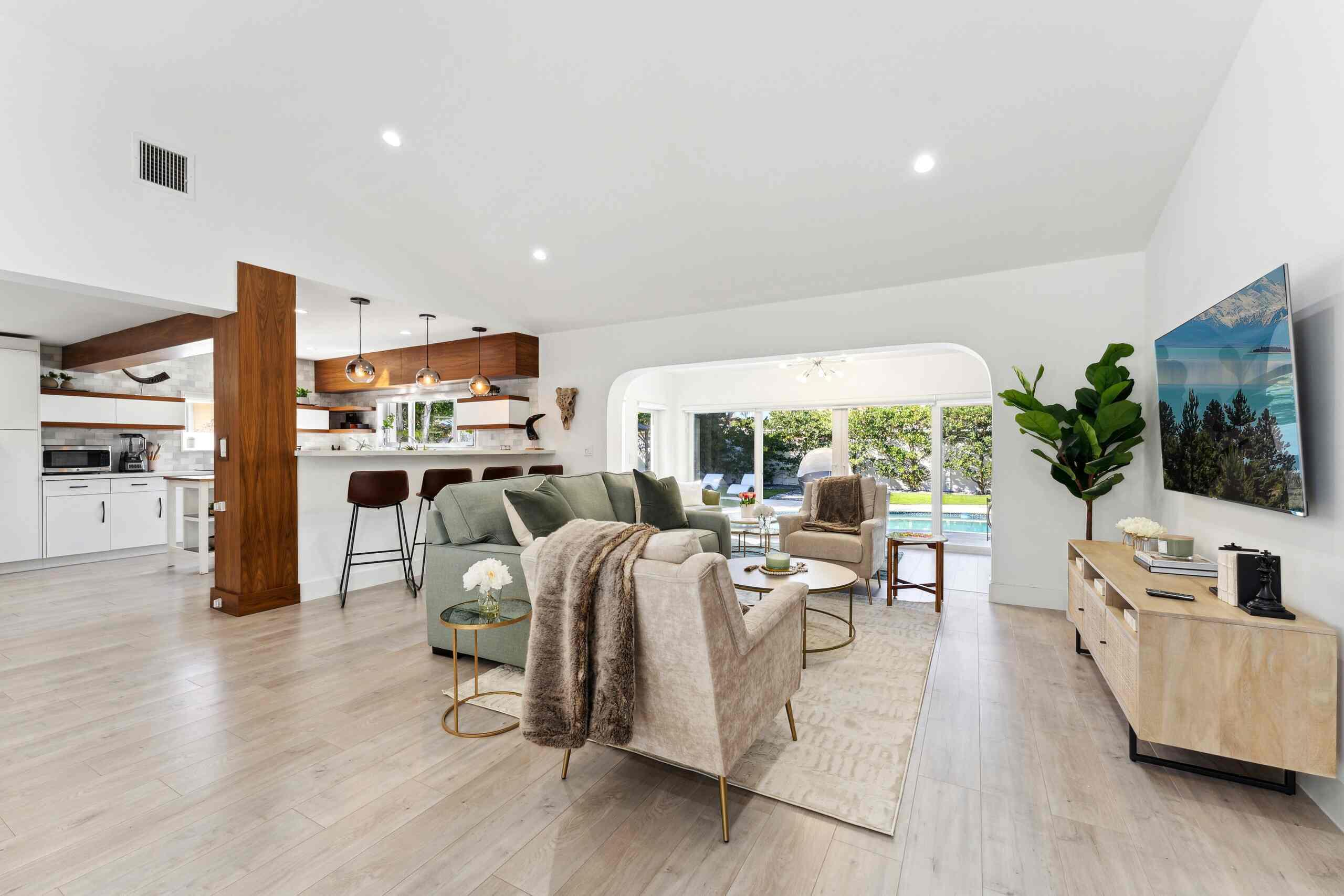 Open-concept living space featuring a wood-finish plank floor, white vaulted ceiling with recessed lighting, and abundant natural light from multiple