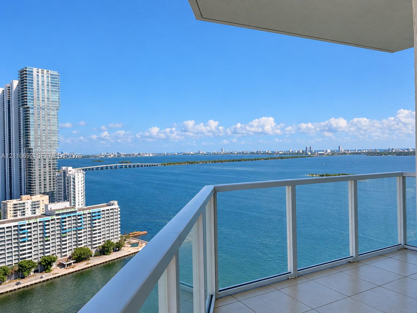 Private balcony featuring glass panel railings and tile flooring, offering expansive water and cityscape scenery
