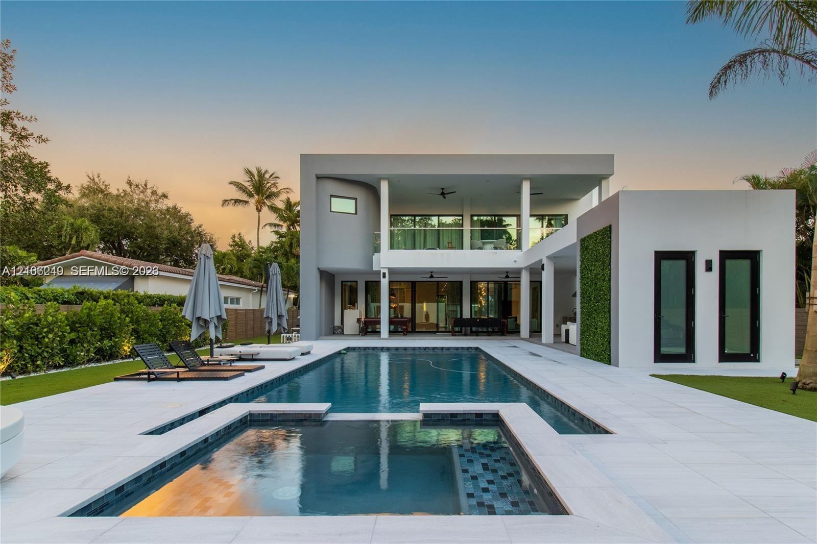 Modern multi-level exterior featuring a glass-railed balcony, ground-level covered patio, integrated pool and spa, and vertical green wall accents