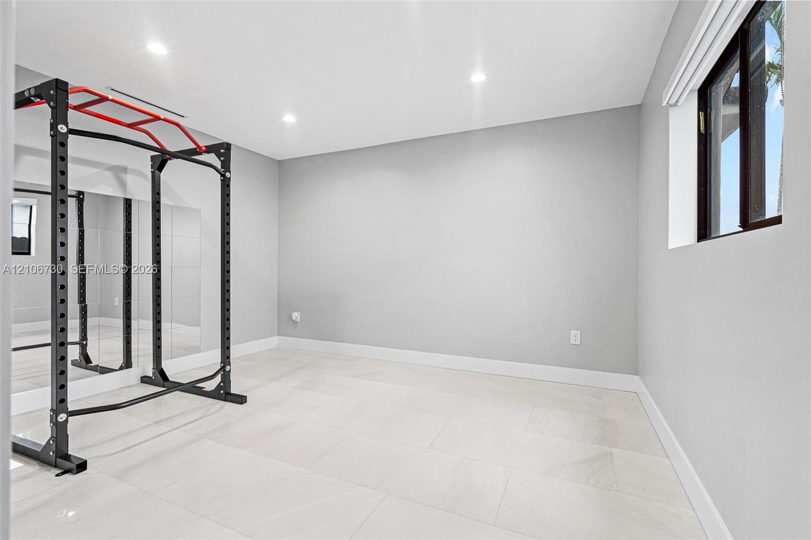 Neutral interior space featuring large-format light-tone tile flooring, recessed ceiling lighting, a floor-to-ceiling wall mirror, and a single window
