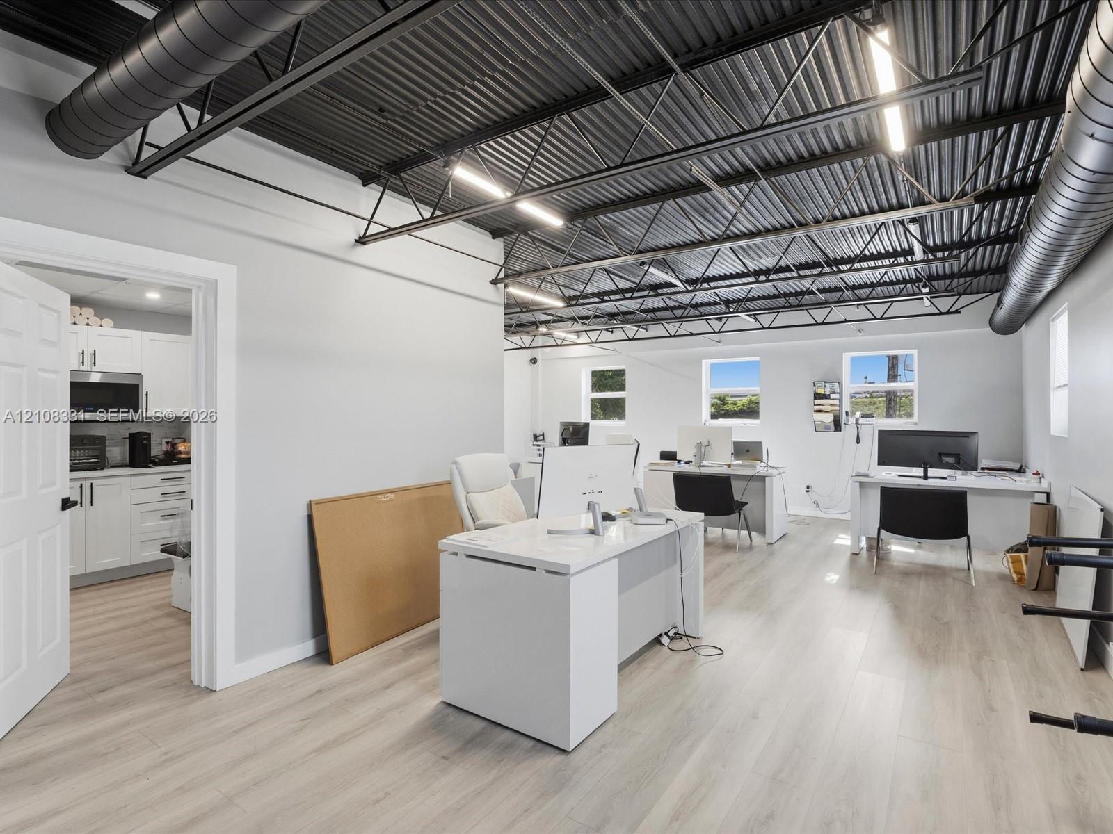 Open-concept space featuring an exposed black corrugated metal ceiling with industrial ductwork, linear LED lighting, wood-finish flooring, and white 