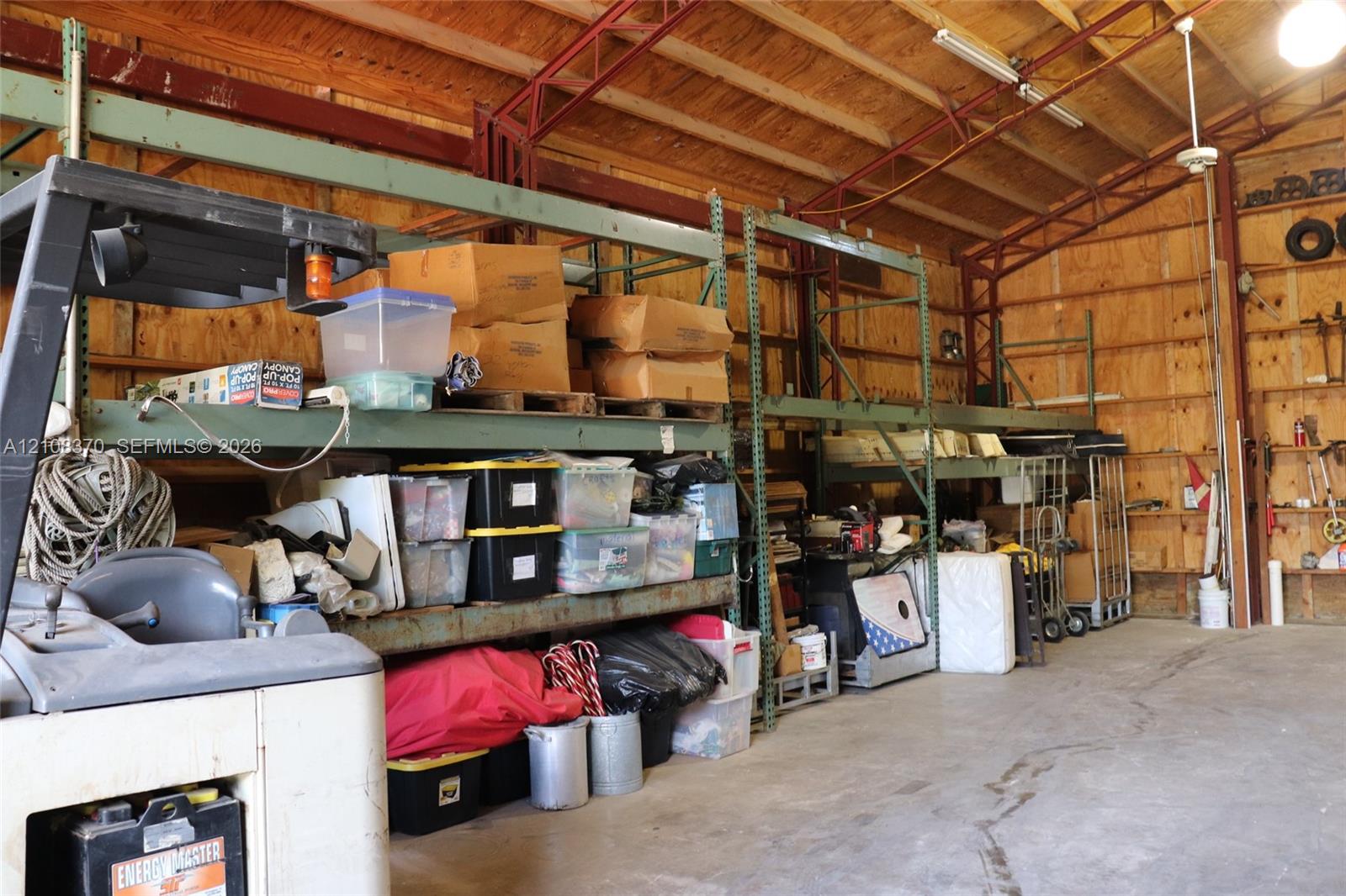 Industrial workspace featuring high-clearance exposed truss ceilings, concrete flooring, and built-in steel warehouse shelving units