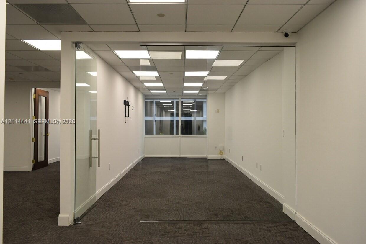 Interior office space featuring floor-to-ceiling glass panel walls, a glass swing door with metal hardware, drop ceiling with recessed panel lighting,