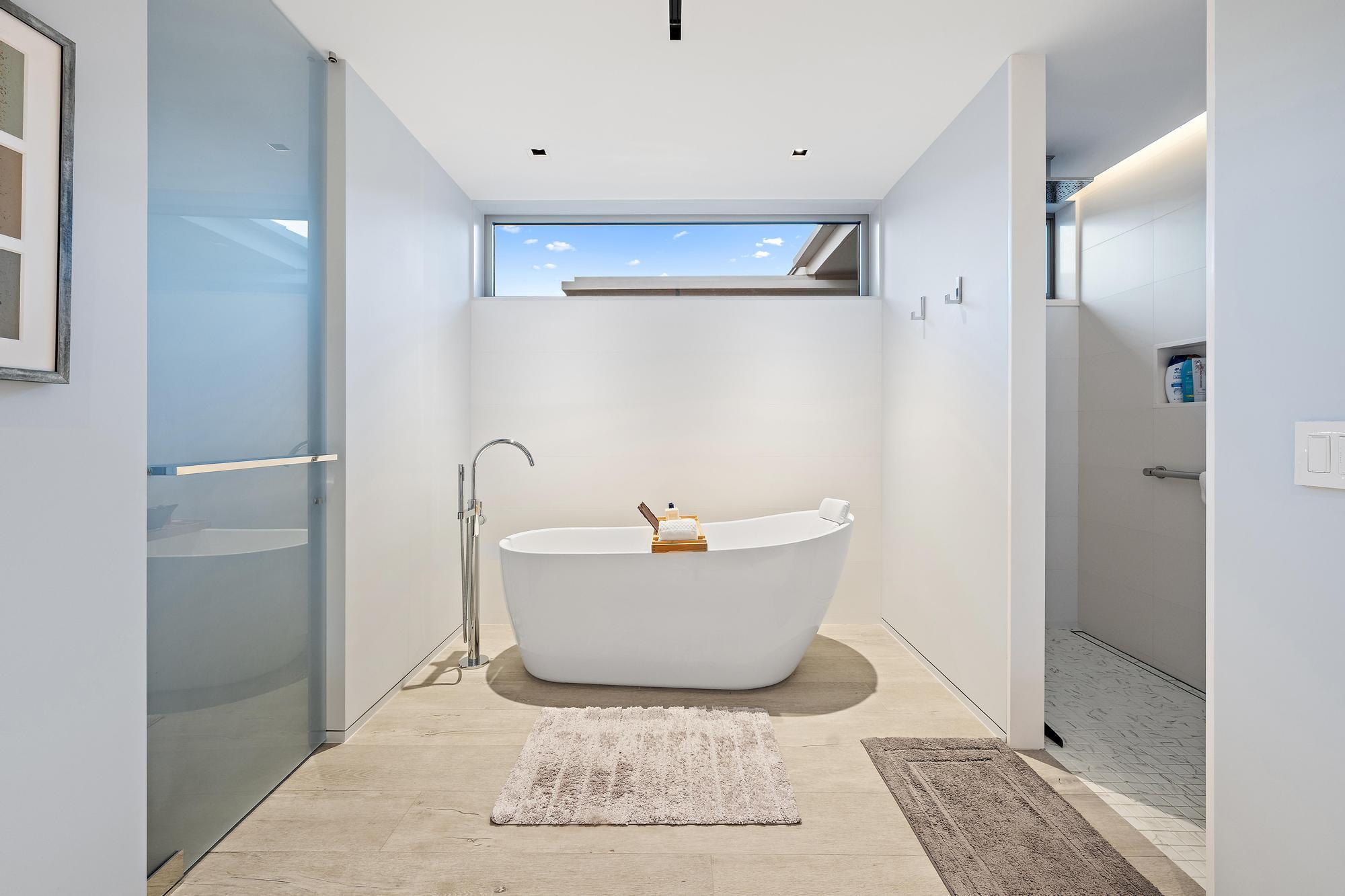 Freestanding soaking tub with floor-mounted faucet, frosted glass shower enclosure, and transom window