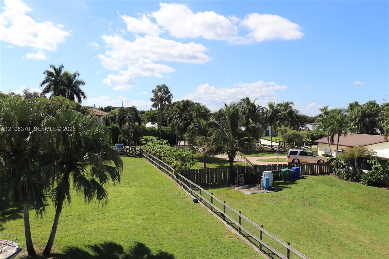 Expansive grassy lot featuring mature palm trees and perimeter wood-rail fencing