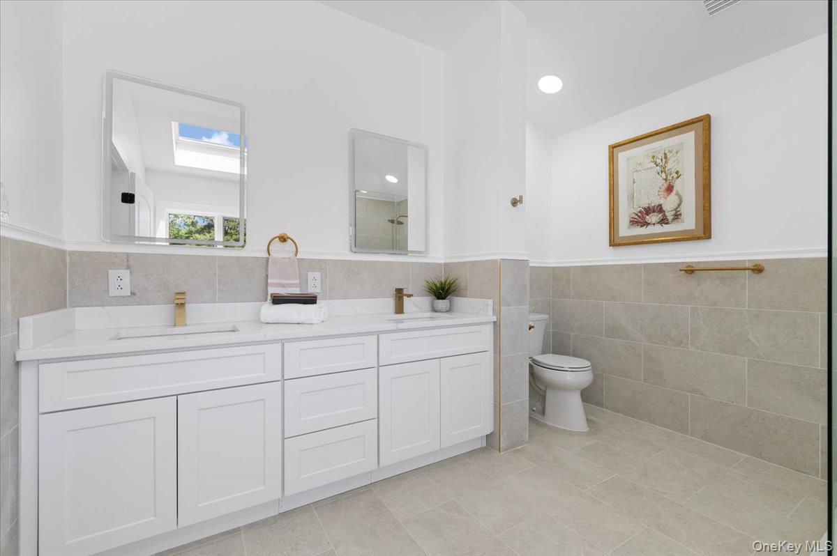 Full bathroom featuring tile walls, double vanity, tile patterned floors, a wainscoted wall, and a skylight