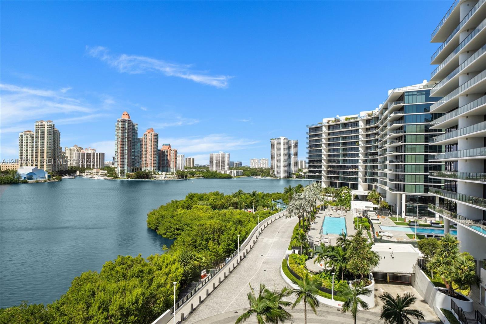 High-rise architecture with expansive glass-railed balconies, waterfront location, multi-level swimming pools, and landscaped grounds with mature palm
