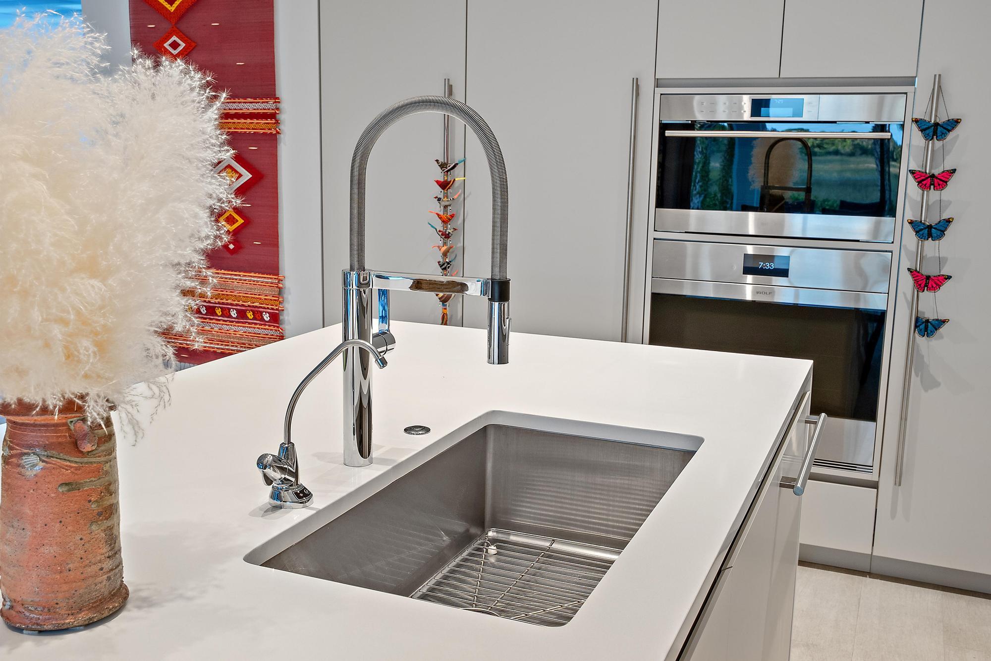 Integrated stainless steel sink with a high-arc faucet, solid surface countertop, and built-in double ovens