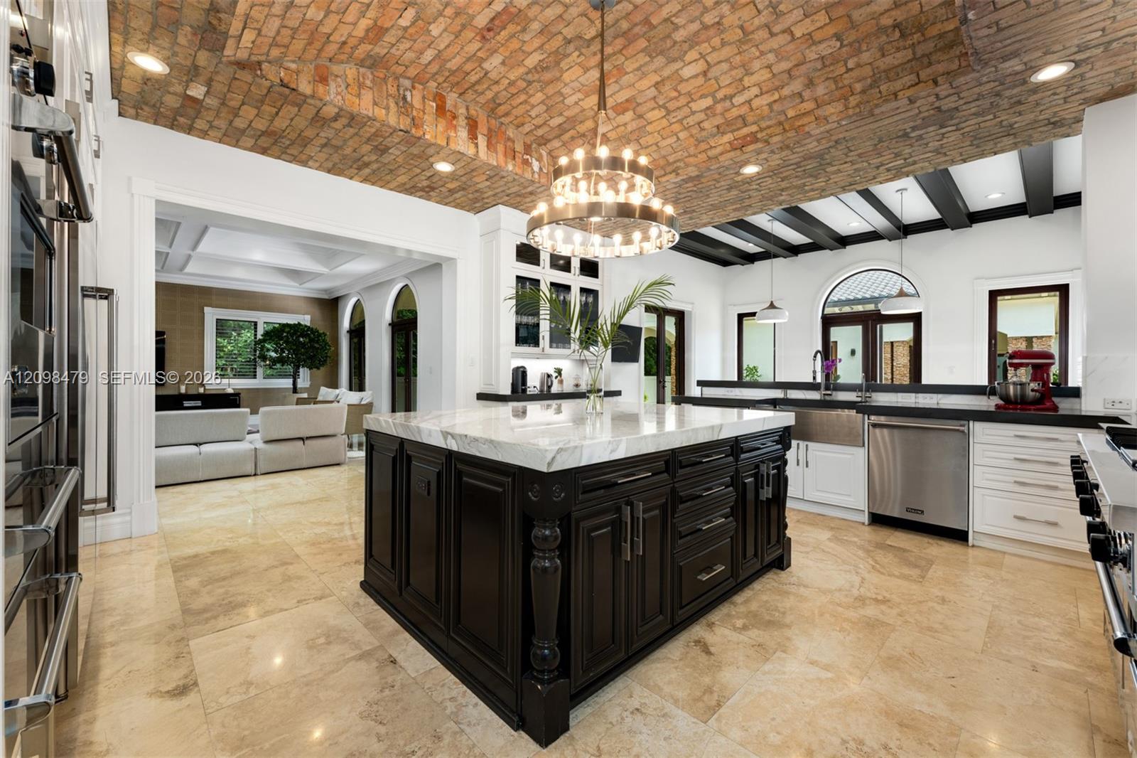 Vaulted brick ceiling, large central island with light-toned countertop, stainless steel appliances, dark wood island cabinetry, and light-toned floor