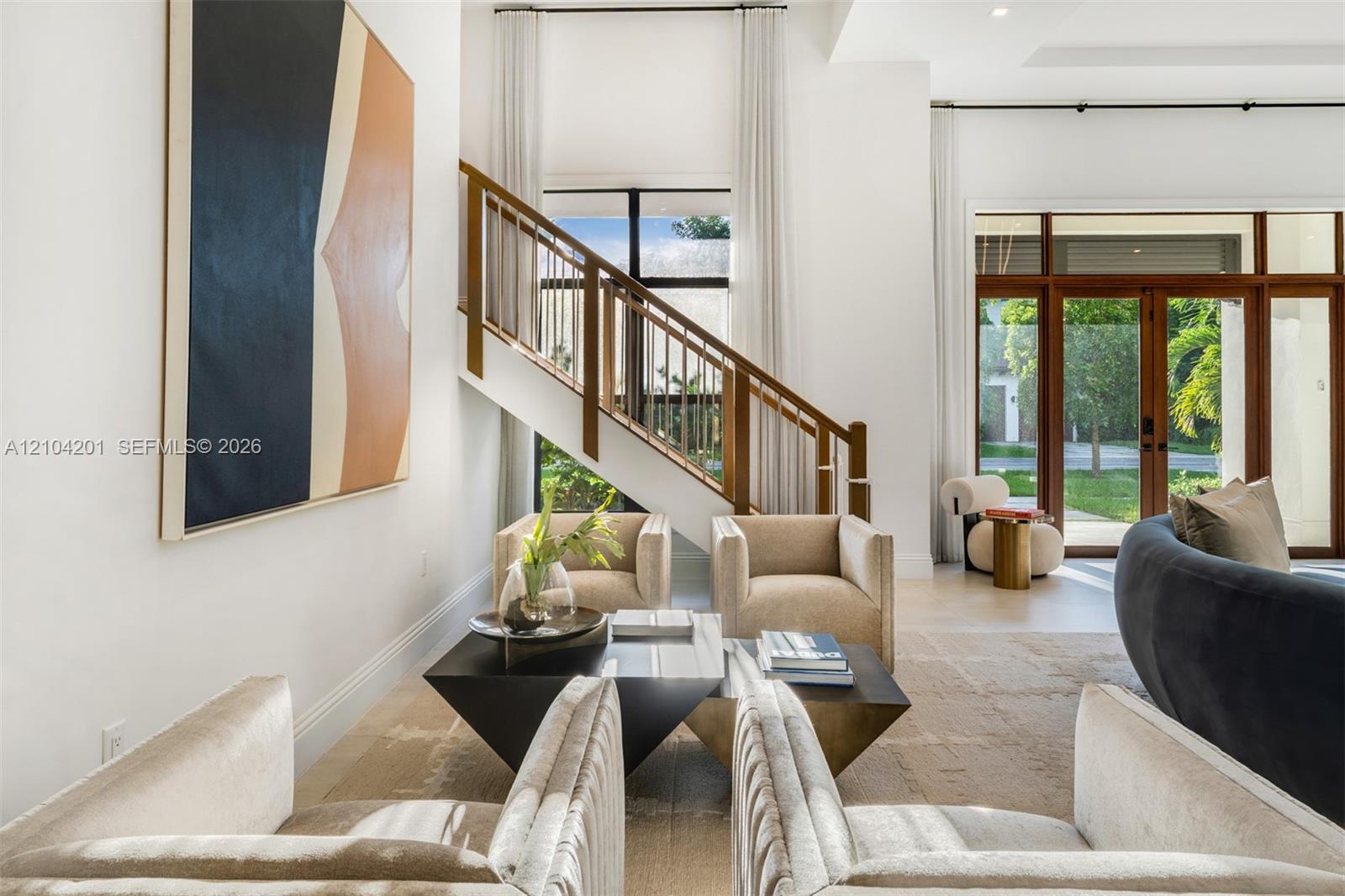 High-ceilinged room featuring a wooden staircase with metal balusters, large-format glass double doors with transom windows, and light-toned flooring