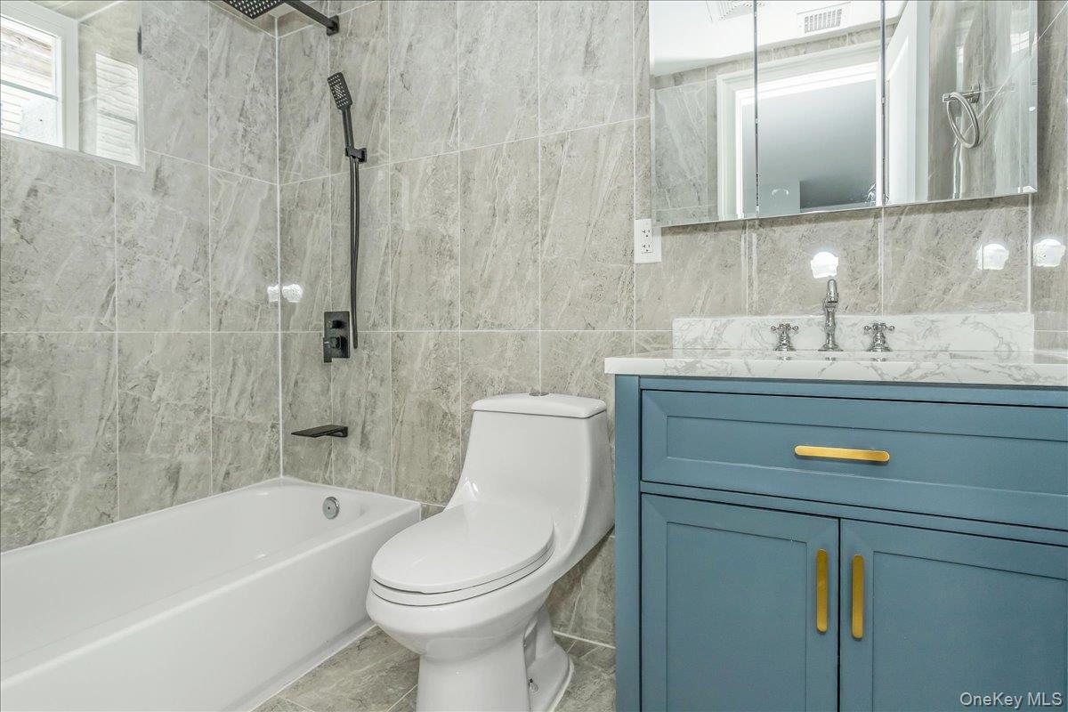 Full bathroom featuring bathing tub / shower combination, vanity, tile walls, and tile patterned flooring