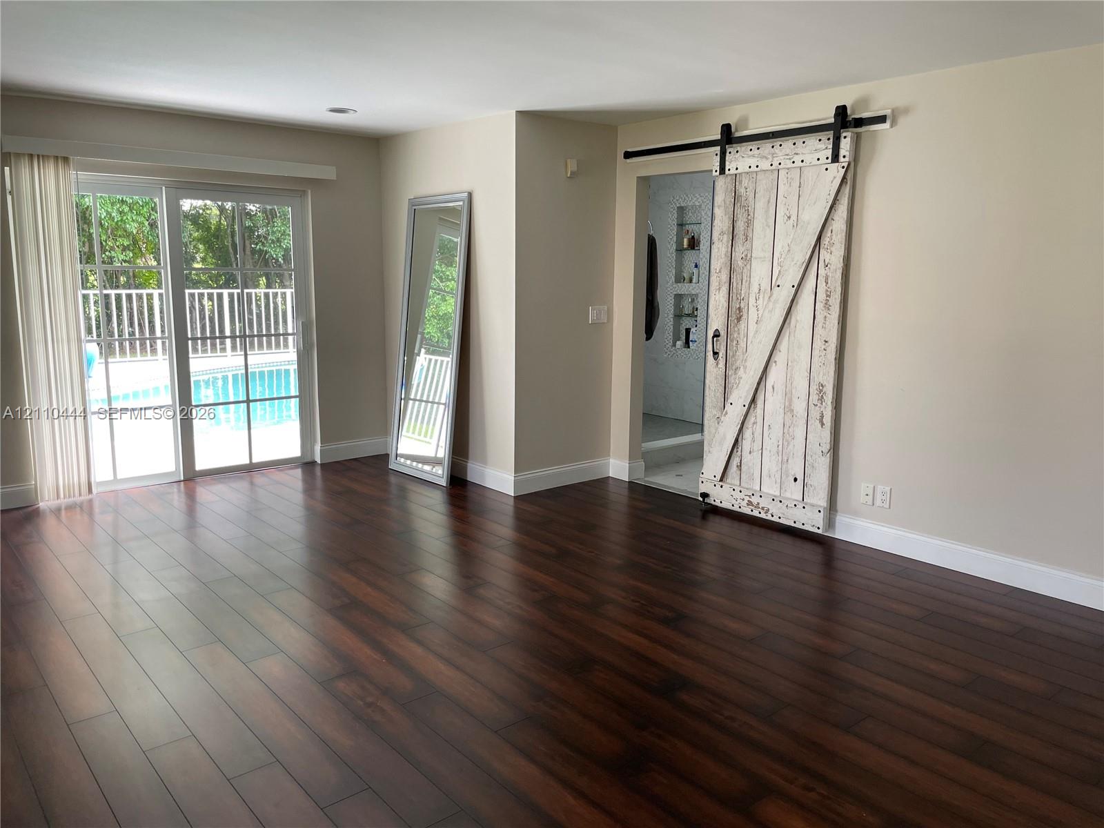 Dark wood-finish flooring, sliding glass door with exterior pool access, and distressed white-finish barn door with matte black hardware