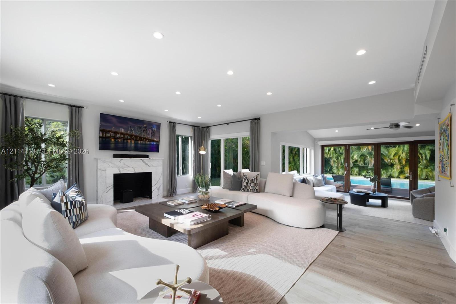 Open-concept living space featuring wood-finish flooring, recessed lighting, a stone-surround fireplace, and multi-panel glass doors