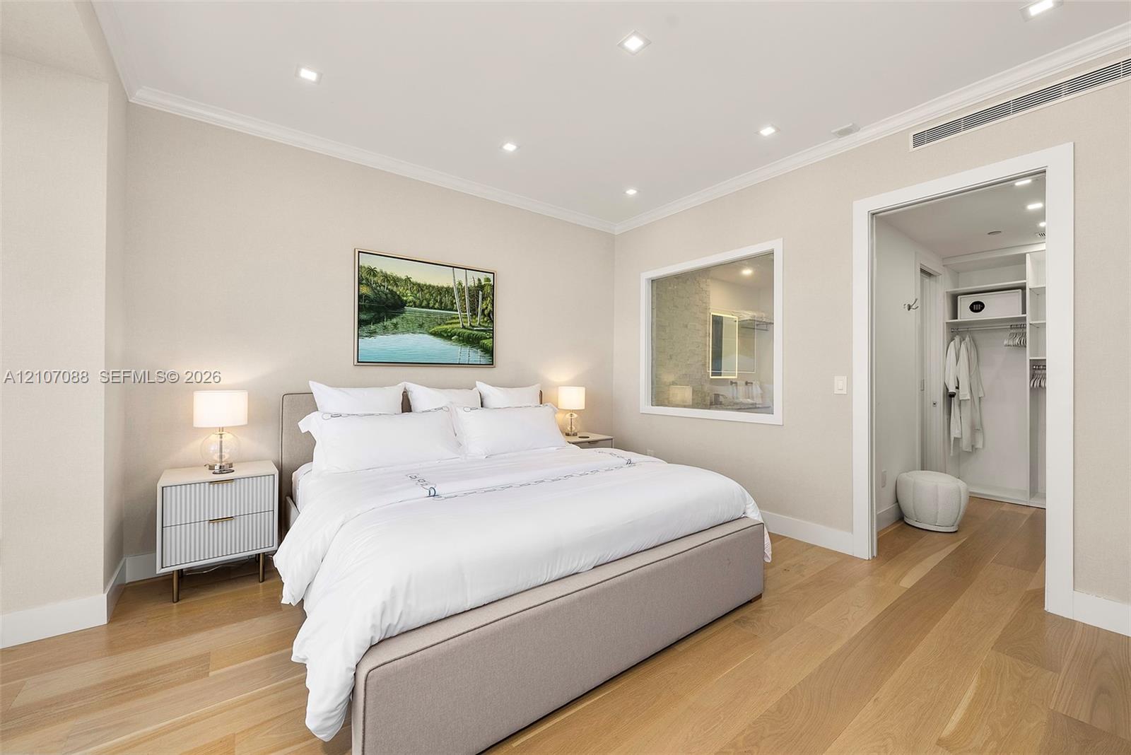 Neutral-toned bedroom featuring light wood-finish flooring, recessed ceiling lighting, crown molding, and an interior window to bathroom with switchab