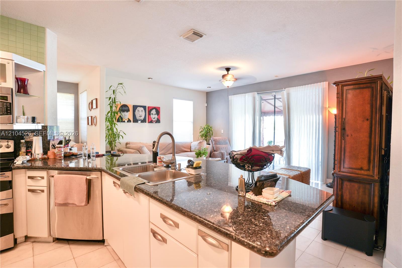 Kitchen featuring a peninsula with stone-finish countertops, stainless steel undermount sink, built-in stainless steel dishwasher, and white cabinetry